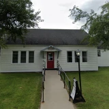 A simple, vinyl sided structure with concrete ramp to the red door